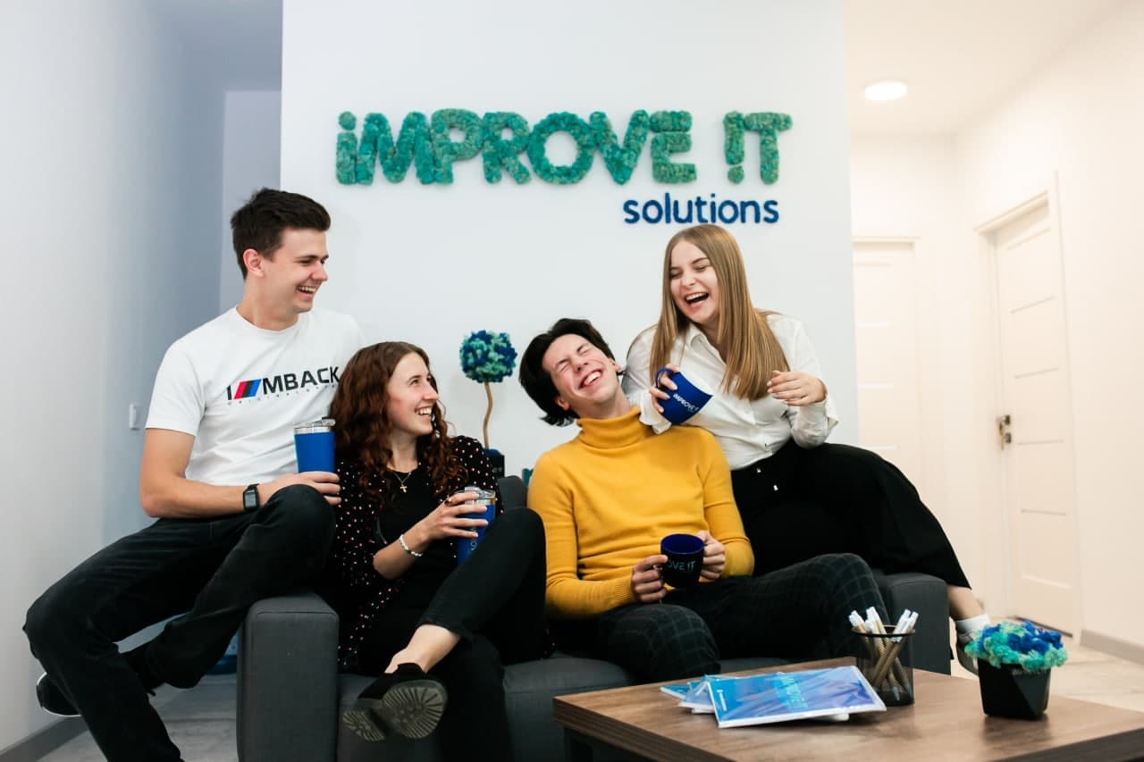 Four ImproveIT colleagues laughing on a sofa beneath the company sign